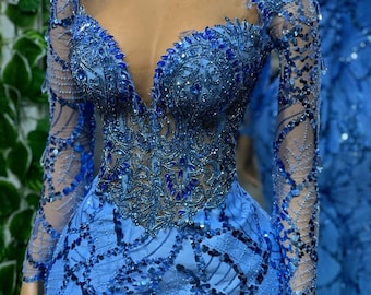 May include: A long-sleeved, light blue dress with a plunging neckline and intricate beading. The dress is made of a sheer fabric with a fitted silhouette.