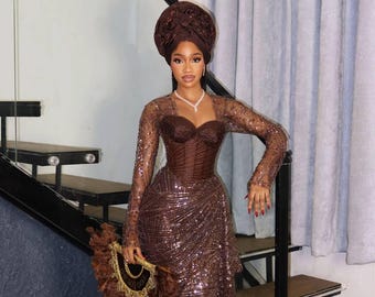 Puede incluir: Un vestido de noche marrón con lentejuelas, mangas largas y un corpiño estilo corsé. El conjunto incluye un turbante a juego y un abanico decorativo. El vestido es largo hasta el suelo y presenta una falda drapeada. El estilo general es elegante y formal.