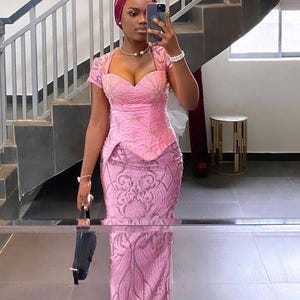 Puede incluir: Una mujer con un vestido rosa con un corpiño ajustado y una falda fluida. El vestido está adornado con lentejuelas y cuentas. Lleva un turbante rosa y un collar de perlas.