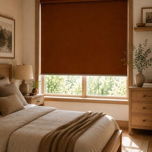 Può includere: Una tenda a rullo color ruggine installata all'interno di un telaio di finestra in legno. La tenda è realizzata in un tessuto solido e opaco che copre il vetro della finestra, bloccando la luce e mantenendo una forma rettangolare pulita.