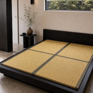 May include: A low-profile black wooden bed frame featuring four rectangular tatami mats arranged in a grid pattern. The mats are made of woven straw with a light tan colour and are bordered by dark fabric trim with a subtle geometric pattern.
