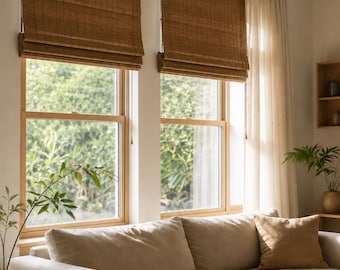 May include: Two brown woven bamboo roll-up shades are mounted on a wooden curtain rod above two windows. A long, light beige sofa with a matching throw pillow sits in front of the windows, which are also dressed with sheer white curtains.