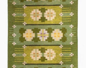 May include: A rectangular green rug with a geometric pattern. The rug features alternating bands of lighter and darker green, with floral and cross-shaped designs in yellow, white, and purple. The rug measures approximately 48 inches long and 30 inches wide.
