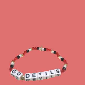 May include: A red, black, and gold beaded bracelet with white letter beads spelling out "GO DEVILS".