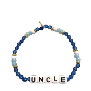 Könnte beinhalten: Ein blaues Perlenarmband mit dem Wort "UNCLE" in weißen Buchstabenperlen. Das Armband hat eine Mischung aus blauen, weißen und goldfarbenen Perlen und ist ein stilvolles Accessoire.