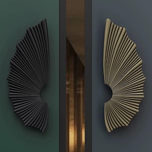 Puede incluir: Dos tiradores decorativos para armarios, uno negro y otro dorado, cada uno con un diseño en forma de abanico. Los tiradores están montados sobre una superficie verde oscuro y gris azulado oscuro, respectivamente. El diseño del abanico presenta una serie de líneas curvas y paralelas que irradian desde un punto central.