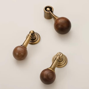 May include: Three antique-style cabinet pulls. Each pull features a dark brown wooden sphere, a brass-colored stem, and a circular base. The pulls are designed for easy installation and add a vintage touch to furniture.