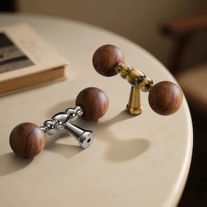 May include: Two decorative cabinet knobs with wooden spheres and metal hardware. One knob has a silver finish, and the other has a brass finish. The knobs are designed for cabinet doors or drawers.