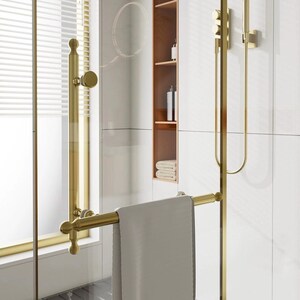 Pode incluir: Um puxador de porta de duche em ouro escovado com um toalheiro horizontal integrado. As ferragens apresentam um design cilíndrico com remates arredondados, montadas numa porta de vidro. Uma toalha cinzenta clara está pendurada na barra.