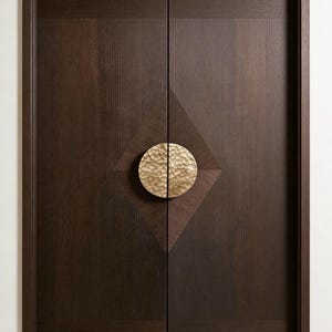 Puede incluir: Un par de puertas de madera marrón oscuro con una incrustación en forma de diamante y un tirador circular dorado martillado. Las puertas tienen un veteado vertical y un diseño simple y elegante.