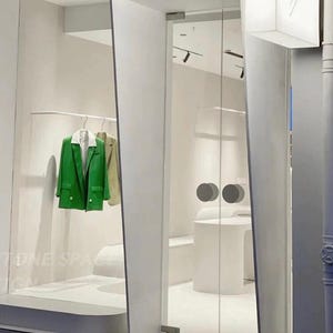 Pode incluir: Vista exterior de uma loja de roupas moderna. Um blazer verde brilhante e um blazer bege estão pendurados em um cabide dentro da loja. A entrada é emoldurada por paredes brancas e portas de vidro.