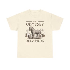 May include: A cream-coloured short-sleeve t-shirt featuring a dark brown graphic of a Trojan horse on wheels in front of a fortress. The text above the horse reads YOU ODYSSEY and the text below the horse reads DEEZ NUTS in a stylised font.