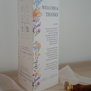 May include: A white card with the words "WELCOME & THANKS" and floral illustrations. The card has text in German and is accompanied by a wax seal, wax beads, and a ribbon.