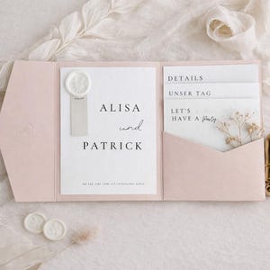 May include: A pale pink tri-fold wedding invitation suite featuring a white card with the text Alisa und Patrick, a wax seal, and three insert cards labeled Details, Unser Tag, and Let's Have a Party, accented with a small dried flower sprig.