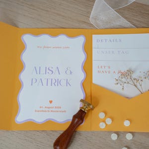 May include: An open orange wedding invitation suite with a white and lavender invitation card. The invitation reads "ALISA & PATRICK" and includes the date August 1, 2026. A wooden handled wax stamp and wax seals are also present.