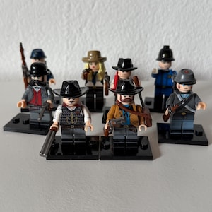 Puede incluir: Un conjunto de minifiguras de Lego que representan personajes con atuendos del oeste. Las figuras incluyen vaqueros, agentes de la ley y una mujer, cada uno con accesorios detallados como sombreros, armas y chalecos. Se encuentran sobre placas base negras.