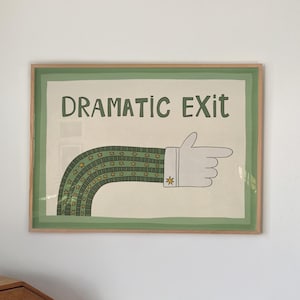 May include: A framed wall art print featuring the text DRAMATIC EXIT in dark green letters above a graphic of a long, curved arm with a green and white striped sleeve and a white glove pointing to the right, accented with a small yellow star.