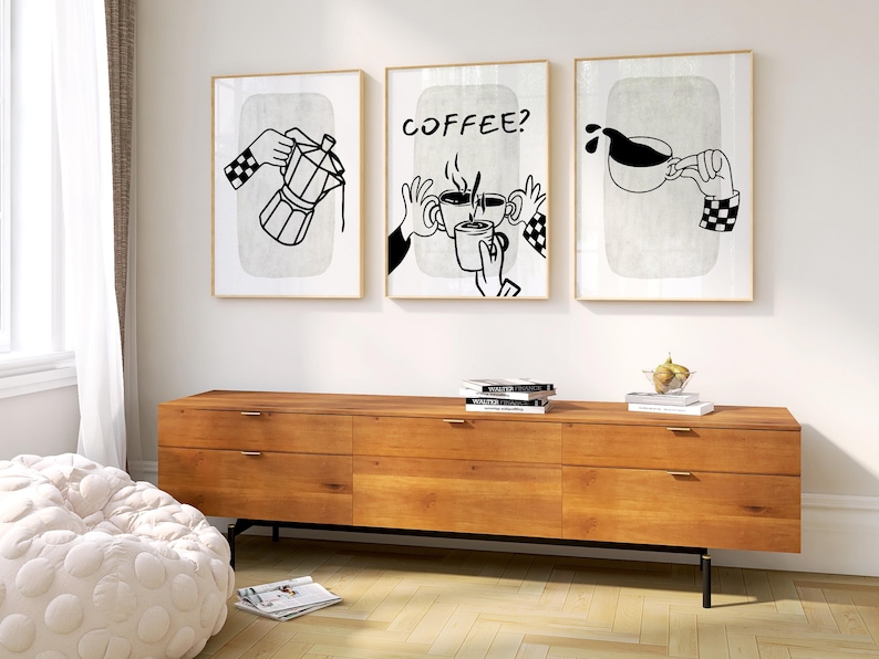 May include: Three framed art prints with coffee-themed illustrations. Each print features black and white line drawings of hands interacting with coffee-making tools and cups. The middle print has the word "COFFEE?" in bold letters. The frames are gold-colored.