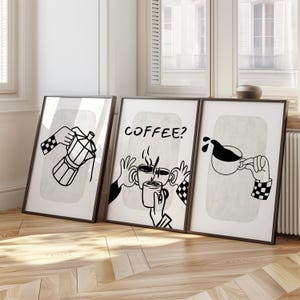May include: Set of three framed art prints with black and white coffee-themed illustrations. One shows a coffee maker, another asks "COFFEE?" and the third depicts coffee pouring into a cup. Each image features hands with checkered sleeves.