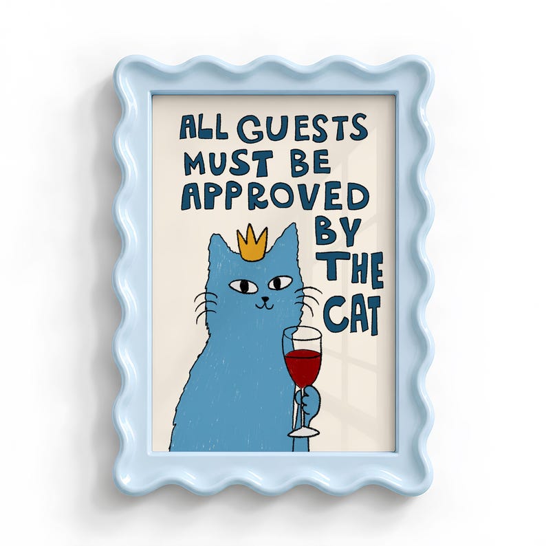 May include: A light blue wavy frame containing a print of a blue cat wearing a yellow crown and holding a glass of red wine. The text reads: ALL GUESTS MUST BE APPROVED BY THE CAT. The background of the print is a light cream color.