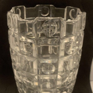 May include: A clear glass vase with a geometric pattern. The vase has a wide mouth and a narrow base. The pattern is made up of squares and circles.
