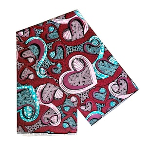 Puede incluir: Tela estampada en rojo, rosa y azul con un diseño de corazones. La tela está etiquetada como "Original Wax Cotton Poplin".