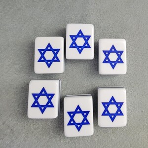 May include: Six white rectangular tiles with a blue Star of David design. The tiles are arranged in a circular pattern against a gray background. The Star of David is a six-pointed star, a symbol of Judaism.