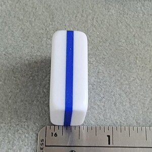 May include: A white rectangular object with a vertical blue stripe down the center. The object is next to a ruler, and appears to be approximately 1 inch in length.