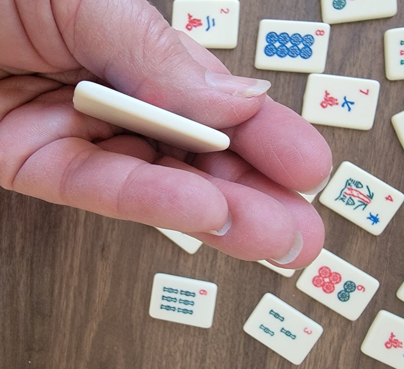 Peut inclure: Une main tenant un jeton blanc avec une surface vide. Le jeton est utilis&eacute; pour jouer au mahjong, un jeu de tuiles chinois.