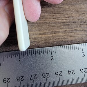 以下が含まれることがあります： 長さ約2.5cmの白い長方形のギターピックです。