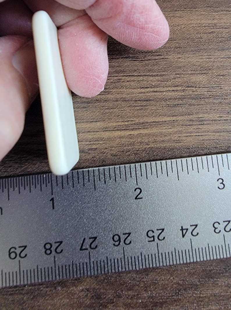 以下が含まれることがあります： 長さ約2.5cmの白い長方形のギターピックです。
