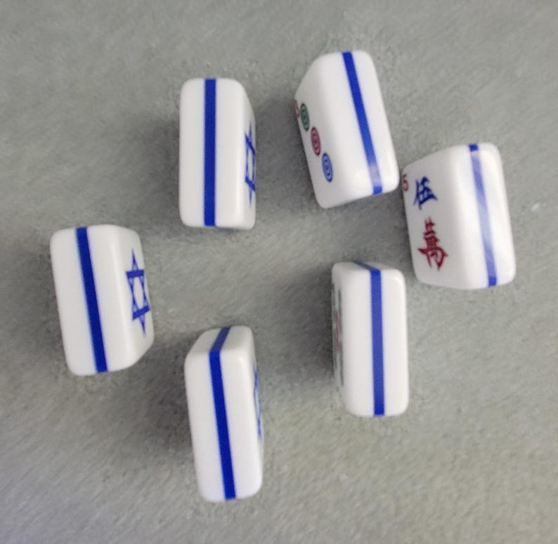 May include: Six white Mahjong tiles with blue vertical stripes and various symbols and characters. Some tiles feature a blue Star of David. The tiles are arranged on a gray surface.