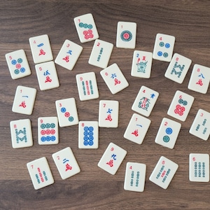 May include: A collection of 28 white tiles with red and blue numbers and symbols. The tiles are arranged in a circle on a brown wooden surface.