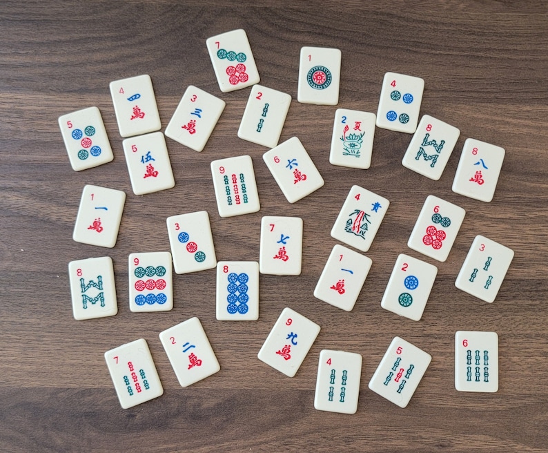May include: A collection of 28 white tiles with red and blue numbers and symbols. The tiles are arranged in a circle on a brown wooden surface.