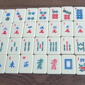 May include: A set of 36 white mahjong tiles with red, blue, and green symbols. The tiles are arranged in rows and columns, with each tile numbered 1 through 9. The tiles are used in the Chinese game of mahjong.