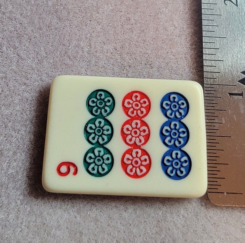 May include: A white domino tile with the number 6 on the left side and three sets of three flowers in green, red, and blue on the right side.