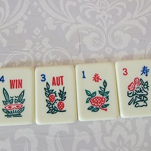 以下が含まれることがあります： 黒と赤の数字と記号が書かれた白いドミノが4つあります。ドミノは左から右に並んでいます。最初のドミノには数字の4と「WIN」という言葉が書かれています。2番目のドミノには数字の3と「AUT」という言葉が書かれています。3番目のドミノには数字の1と中国語の文字が書かれています。4番目のドミノには数字の3と中国語の文字「春」が書かれています。