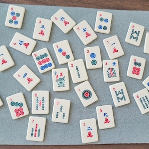 May include: A set of 18 white tiles with black and red numbers and symbols. The tiles are arranged in a random pattern on a brown wooden surface. The tiles are used for the game of Mahjong.