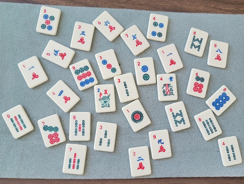 May include: A set of 18 white tiles with black and red numbers and symbols. The tiles are arranged in a random pattern on a brown wooden surface. The tiles are used for the game of Mahjong.