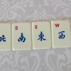 以下が含まれることがあります： 赤と青の文字が書かれた白いタイルが4枚。タイルにはN、S、E、Wと表示されています。タイルには青い中国語の文字も書かれています。