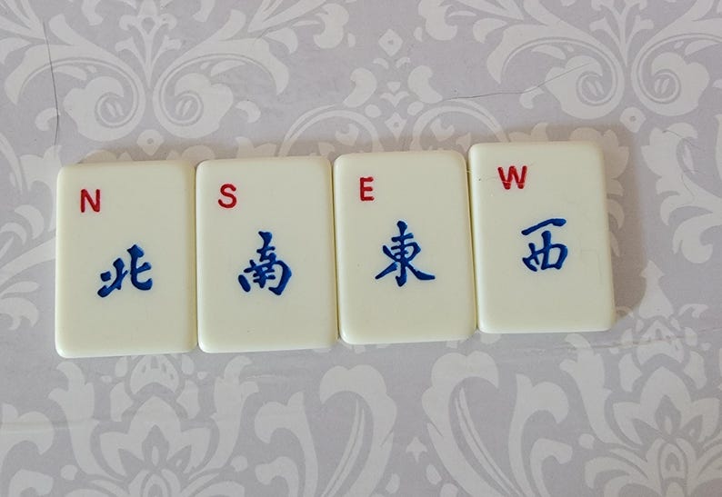 以下が含まれることがあります： 赤と青の文字が書かれた白いタイルが4枚。タイルにはN、S、E、Wと表示されています。タイルには青い中国語の文字も書かれています。