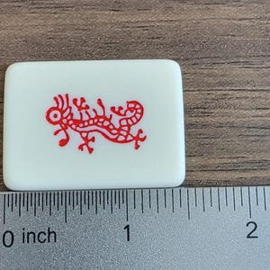 以下が含まれることがあります： 赤い龍のデザインが描かれた白いタイル。タイルの幅は約2.5cmです。