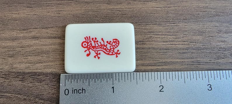 以下が含まれることがあります： 赤い龍のデザインが描かれた白いタイル。タイルの幅は約2.5cmです。