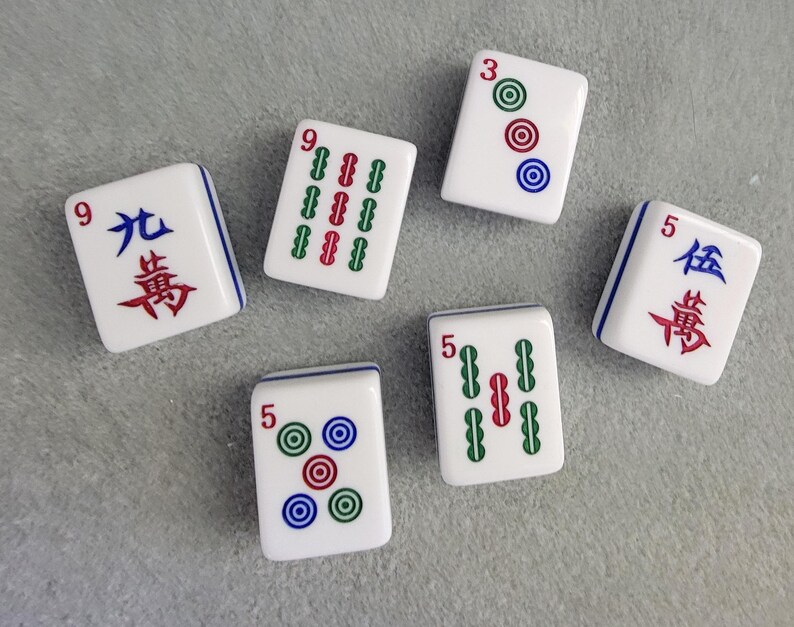 May include: Six white Mahjong tiles with blue borders are arranged on a gray surface. The tiles display various combinations of numbers, Chinese characters, and colored circles and lines. The tiles are for the classic game of Mahjong.