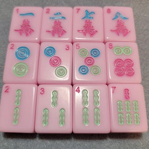 May include: A collection of pink Mahjong tiles with various symbols and numbers in green, blue, and pink. The tiles are arranged in a grid, showcasing the different designs and numbers.