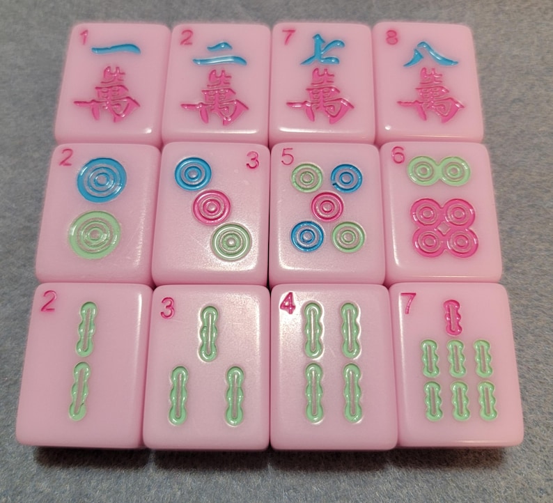May include: A collection of pink Mahjong tiles with various symbols and numbers in green, blue, and pink. The tiles are arranged in a grid, showcasing the different designs and numbers.