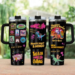 May include: Three black insulated tumblers with handles and straws. Each tumbler features colorful graphics and text, including "Best in Dungeon," "Princess Donut & Mongo," and "Goddamnit Donut!" The tumblers have a stainless steel rim and a black lid.