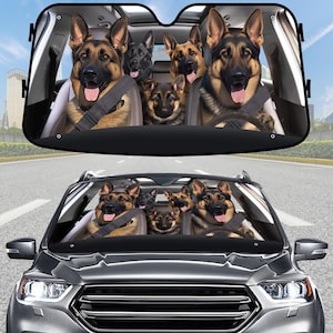 Op de afbeelding: Een auto zonnescherm met een grappig ontwerp van Duitse Herders in een auto. De honden dragen veiligheidsgordels en lijken te rijden. Het zonnescherm is zwart met een full-color afbeelding van de honden.