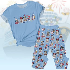 May include: Pale blue pajama set comprising a short-sleeved t-shirt and trousers. The t-shirt features cartoon characters in sailor outfits. The trousers have a repeating pattern of the same characters. The set is made of a soft material.