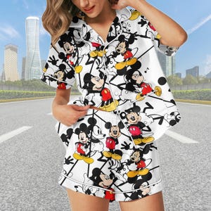 May include: White pajama set with a repeating Mickey Mouse pattern. The short-sleeved top and shorts have white piping and buttons. Mickey Mouse's red shorts, yellow shoes, and black features are visible throughout the design.